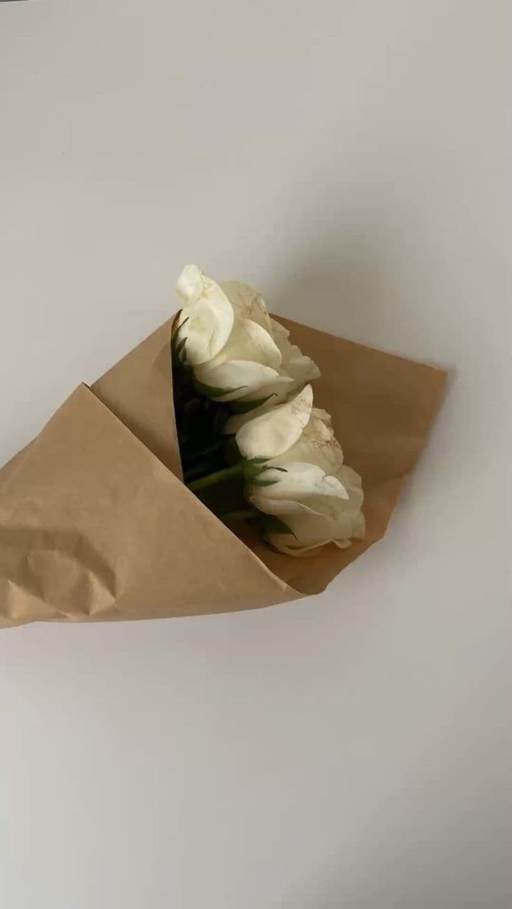 Tres rosas blancas envueltas en papel kraft, sostenidas en una mano