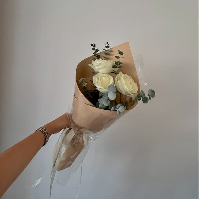Pequeño ramo de rosas blancas con envoltura simple, sostenido en una mano