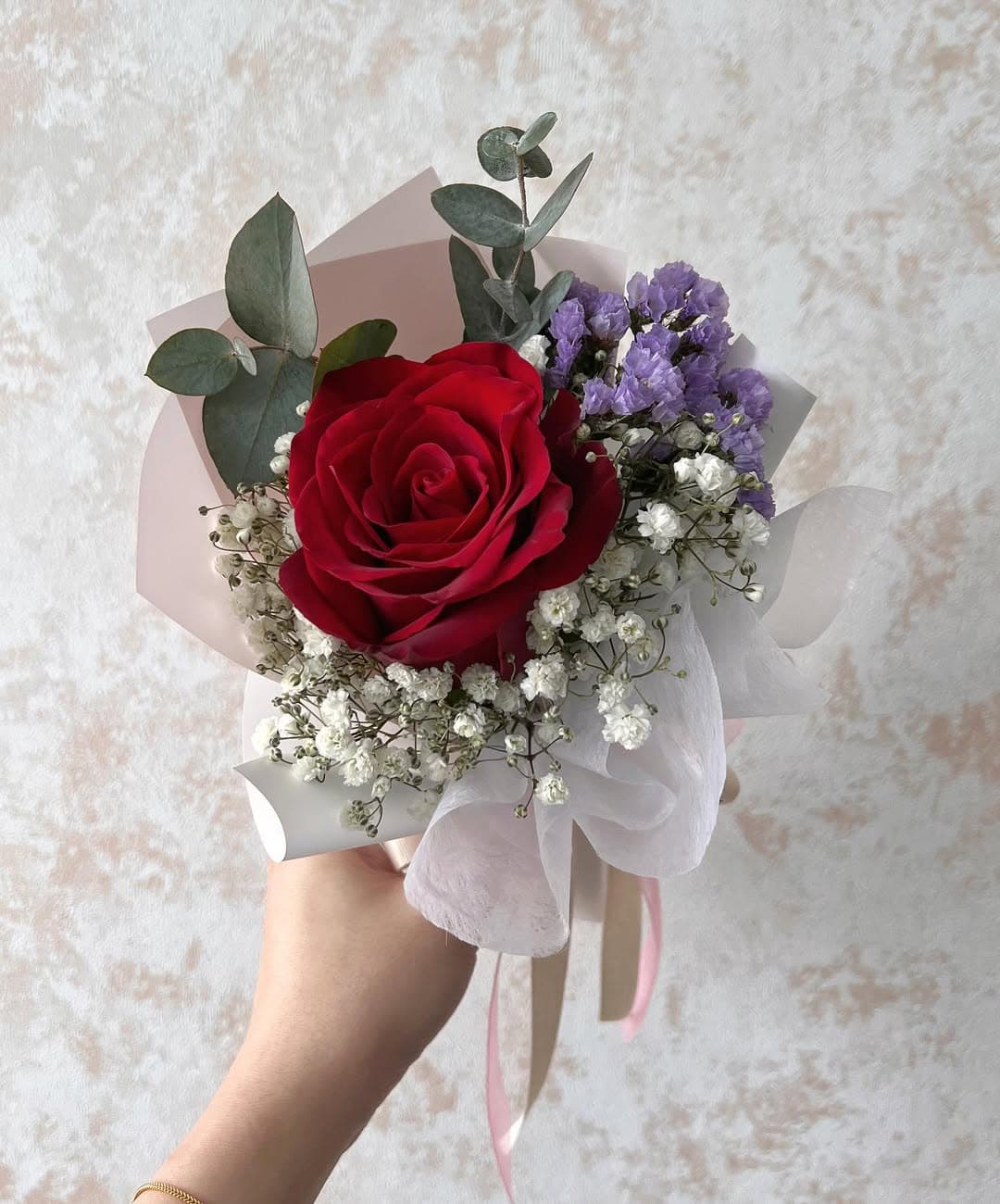 Una sola rosa roja con hojas verdes envuelta simplemente